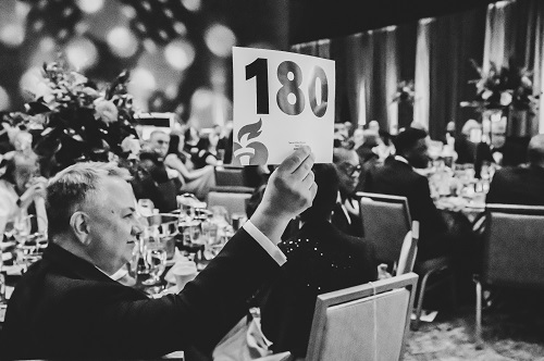 Black and white photo of a man holding up paddle number 180